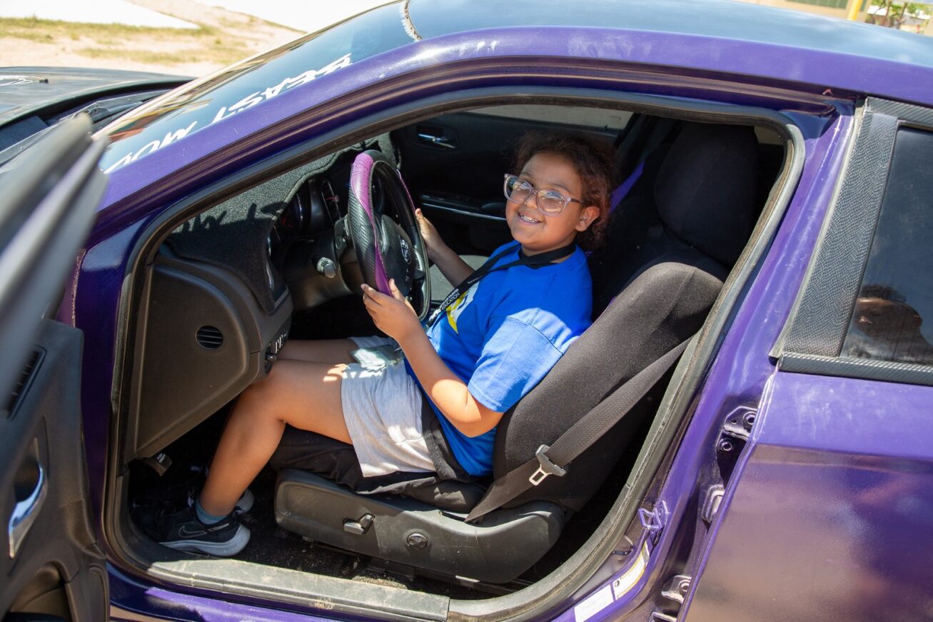 A student smiles behind the wheel of a purple car for Career Day