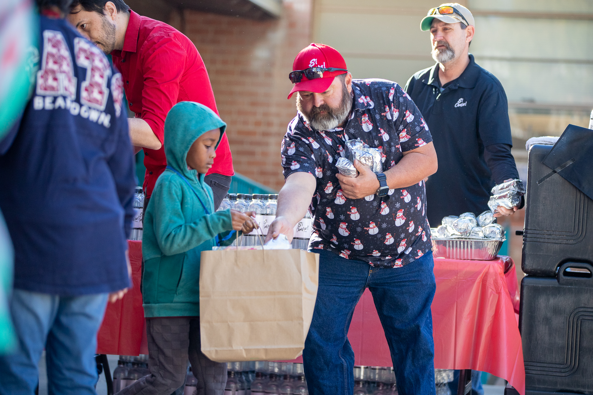 A man in a snowman shirt puts a wrapped burrito into a boy's paper bag