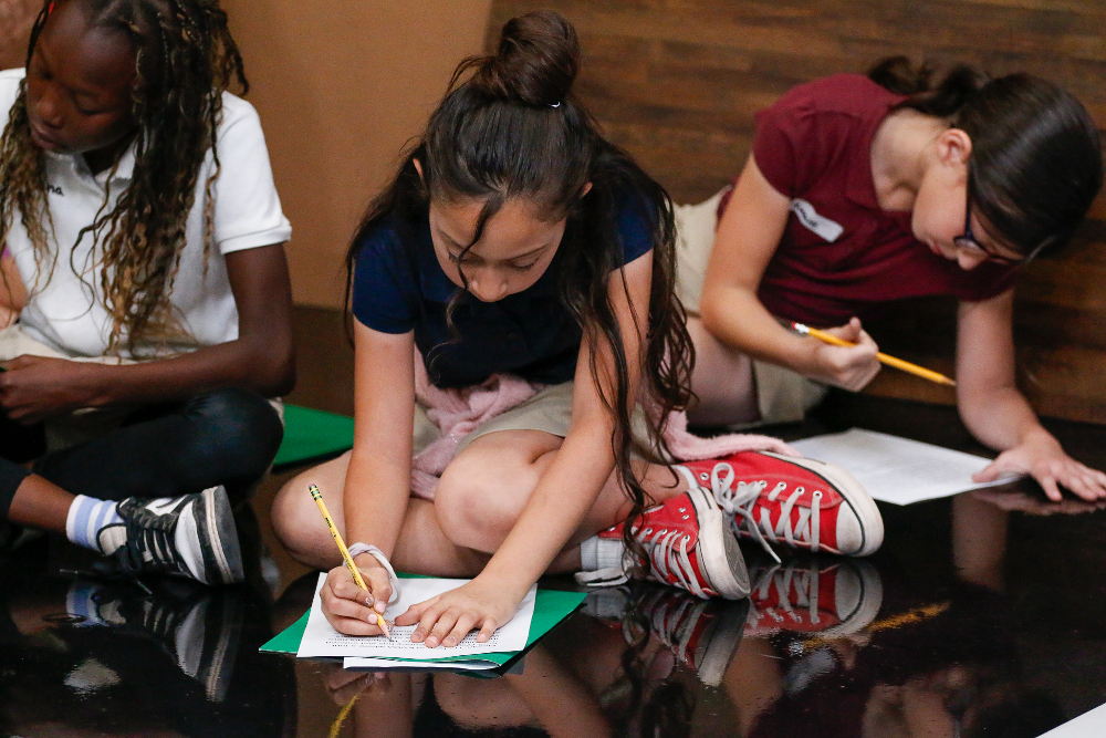 Three girls sit on the floor taking notes