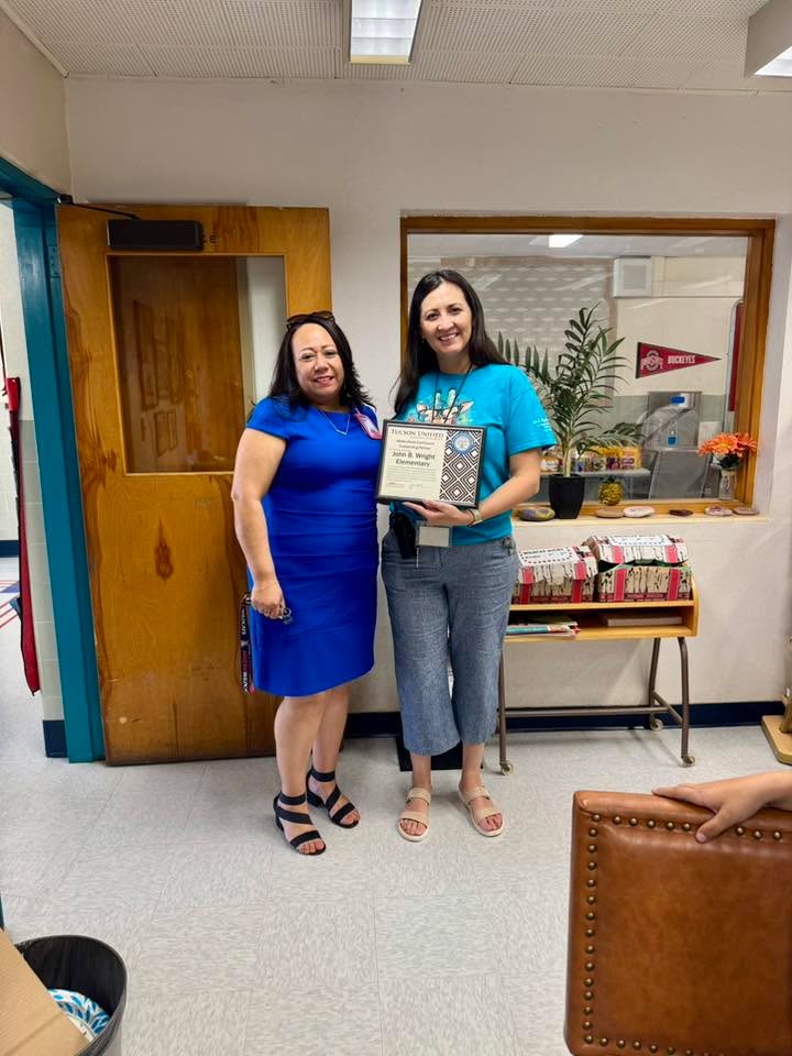 Two women smile holding a certificate in the front office