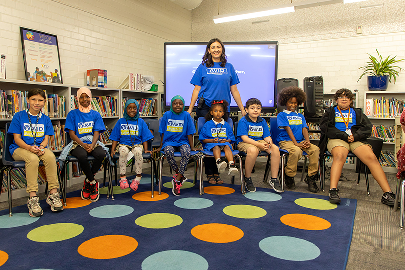 Students in blue AVID Ambassador shirt sit in a row with their principal behind them