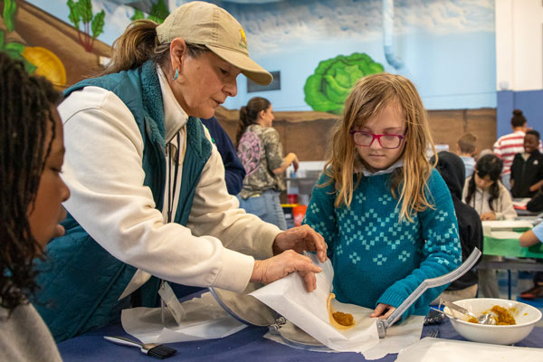 An instructor helps children learn to fold the empanadas