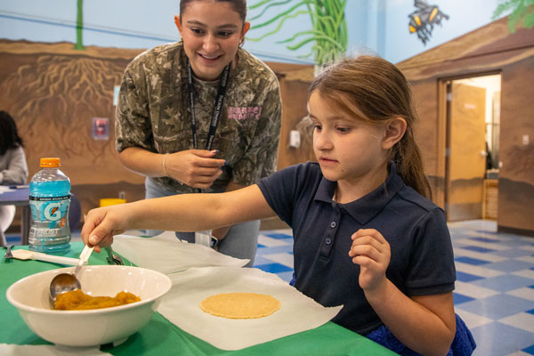 A child carefully scoops filling while be watched by an instructor.