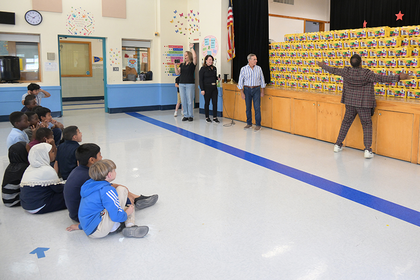 Students sit on the floor looking up at a display of Lego kits on the stage