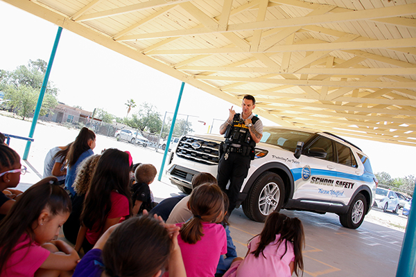 A School Safety officer talks to students outside in front of his vehicle